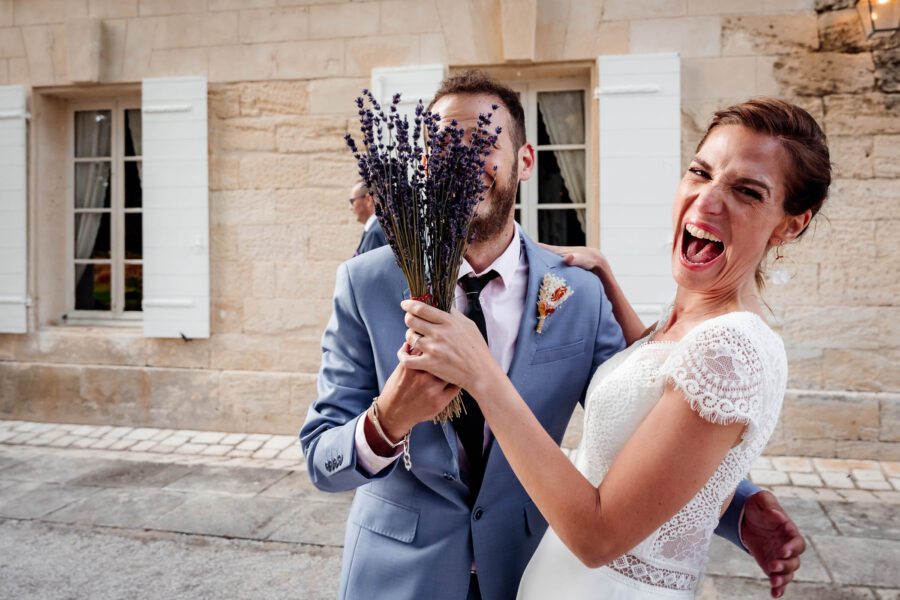 Mariée hilare avec un bouquet de lavande devant un marié caché – mariage dans le Sud de la France